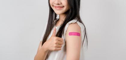 Jeune femme pouce en haut signe après avoir une vaccin. montrant épaule bras avec bandage après recevoir vaccination, troupeau immunité, côté effet, booster dose, vaccin passeport et coronavirus pandémie photo