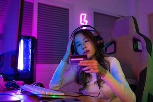 Haut en haut en ligne Jeu avec crédit carte concept. joueur et e-sport en ligne de asiatique femme en jouant en ligne ordinateur vidéo Jeu avec éclairage effet, diffuser diffusion vivre à maison. joueur et e-sport jeu photo