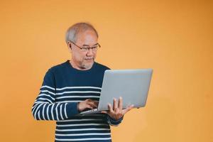 asiatique Sénior homme en utilisant portable ordinateur pour travail après retraite sur le Jaune Contexte. photo