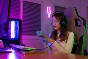 poignet douleur concept. joueur et e-sport en ligne de asiatique femme en jouant en ligne ordinateur vidéo Jeu avec éclairage effet, diffuser diffusion vivre à maison. sa utilisation sa poignet pour une longue temps. photo