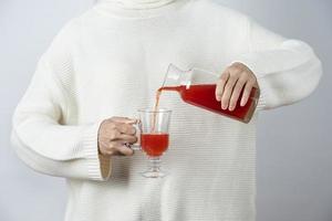 Mains féminines verser le jus de tomate dans une tasse en verre contre un mur gris photo