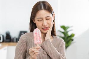 santé asiatique Jeune femme émouvant joue, expression, Souffrance de mal aux dents, pourriture ou sensibilité cavité molaire dent, les dents ou inflammation manger du froid la glace crème à maison. sensible les dents personnes. photo