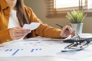 proche en haut main de stress asiatique Jeune employé affaires femme calculer impôt le revenu et dépenses, factures, crédit carte pour Paiement ou jour de paie sur table à Accueil bureau. financier, la finance gens concept. photo