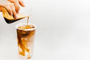 barista verser café dans verre avec la glace dans blanc Contexte. photo