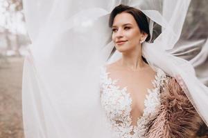 une magnifique portrait de le la mariée en dessous de une voile. élégant femme avec professionnel faire en haut et cheveux style. une photo de délicat de la mariée mains caché en dessous de une voile. mariage journée. mariage. mode la mariée.