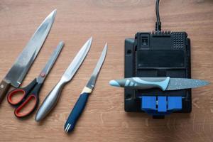 affûtage une couteau sur un électrique taille crayon à maison. flatlay couteau lame, ciseaux, aiguiseurs, poussière mouches sur le machine. photo