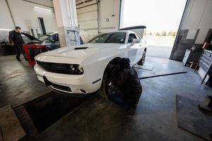 mécanicien dans une station de réparation de service travaillant avec muscle car. un ouvrier soulève la voiture pour diagnostiquer le châssis. photo