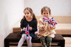 deux sœurs sont assises sur un canapé à la maison avec des drapeaux britanniques sur les mains. grande-bretagne enfants filles avec drapeau. photo