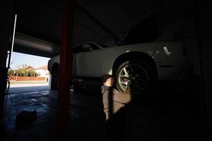 mécanicien dans la station de réparation de service travaillant avec muscle car dans l'ascenseur à l'ombre du coucher du soleil. photo