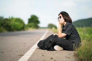 femme assise avec un sac à dos faisant de l'auto-stop le long d'une route dans la campagne photo