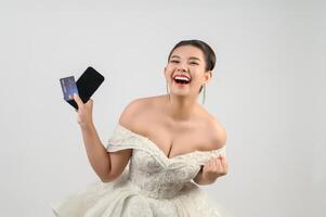 Jeune asiatique magnifique la mariée affectation avec crédit carte et téléphone intelligent dans main photo