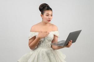 Jeune belle mariée asiatique pose avec un ordinateur portable à la main photo