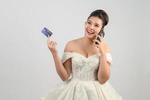 Jeune asiatique magnifique la mariée affectation avec crédit carte et téléphone intelligent dans main photo