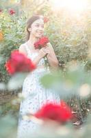 Jeune asiatique femme portant une blanc robe pose avec une Rose dans Rose jardin photo