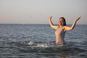 content femme à le mer dans le Soleil. femme dans une maillot de bain éclaboussures l'eau sur une Contexte de vagues. été vacances sur le plage. photo