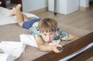 le enfant mensonges sur le lit avec le la télé éloigné contrôle. photo