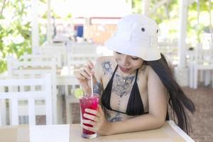 Youn belle et sexy femme en bikini avec jus de fruits frais au restaurant, souriant de bonheur en vacances en été. jolie fille souriante buvant un délicieux cocktail rouge sucré, une journée de détente incroyable photo