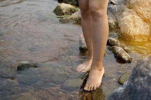 asiatique femme faire un pas pieds nus marcher vers le bas une courant avec très clair l'eau. à côté de le flux, là sont beaucoup grand et petit rochers. doux et sélectif se concentrer. photo