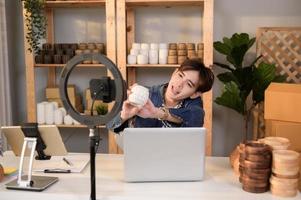 une Jeune asiatique homme entrepreneur vivre diffusion à vente artisanat des produits à les clients dans le sien magasin , La technologie en ligne affaires concept. photo