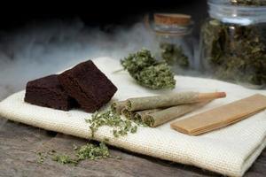 Pré-rouler cannabis les articulations et gâteau Brownies avec guérir cannabis bourgeons dans une clair verre pot pose une noir Contexte photo