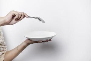 fermer, en portant une blanc assiette et cuillère, isolé sur une blanc Contexte. photo