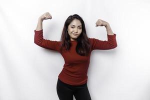 excité asiatique femme portant une rouge Haut montrant fort geste par levage sa bras et muscles souriant fièrement photo