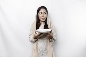 un asiatique musulman femme est jeûne et faim et en portant ustensiles coutellerie tandis que à la recherche de côté en pensant à propos quoi à manger photo