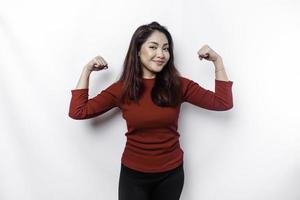 excité asiatique femme portant une rouge Haut montrant fort geste par levage sa bras et muscles souriant fièrement photo