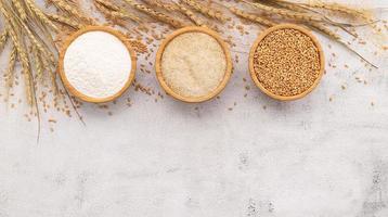 grains de blé, farine de blé brun et farine de blé blanc dans un bol en bois mis en place sur fond de béton blanc. photo