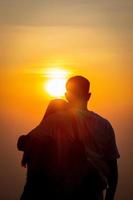 silhouette de une Jeune couple en train de regarder le le coucher du soleil pendant crépuscule sur une haute Montagne et embrassement Heureusement. content couple embrassement chaque autre avec l'amour et relation amicale et la gentillesse pour chaque autre. photo