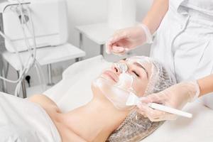 esthéticien s'applique crème masque sur femme visage pour rajeunissement visage peau, procédure dans beauté salon photo