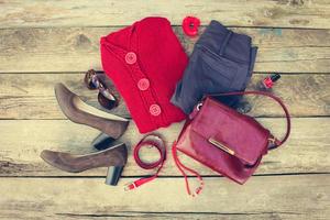 aux femmes l'automne Vêtements et accessoires rouge chandail, pantalon, Sac à main, perles, des lunettes de soleil, clou polonais, cheveux groupe, ceinture sur en bois Contexte. tonique image. photo