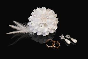 deux mariage anneaux, des boucles d'oreilles de le la mariée et du marié boutonnière sur noir Contexte avec réflexion. mariage symboles photo