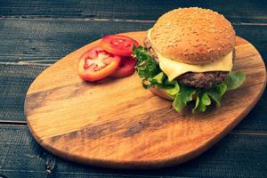 Hamburger fait maison frais et savoureux avec légumes frais, laitue, tomate, fromage à côté de tranches de tomates sur une planche à découper. espace libre pour le texte photo