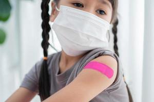 fermer de médicinal plâtre après vacciné dans épaule de asiatique fille des gamins dans hôpital. pédiatre fait du vaccination pour enfants. vaccination, immunisation, maladie la prévention concept. photo