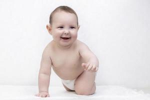 enfant avec une sourire sur une blanc Contexte. une content six mois vieux garçon rampe sur le lit et des rires. conceptuel photo de paternité et maternité.