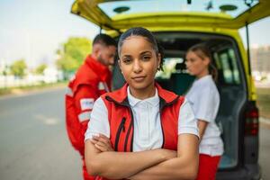 Jeune femelle africain américain paramédical permanent arrière de le ambulance. ambulanciers par le ambulance. deux ambulanciers prise en dehors brancard de ambulance photo