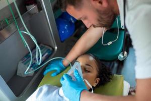 paramédical soins de santé urgence Personnel prise se soucier de une mensonge vers le bas Jeune femme patient sur tendeur avec médical ventilateur système et poche-valve masques à l'intérieur un médical un service ambulance auto. photo