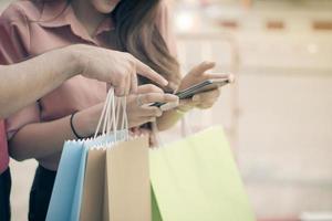 heureux jeune couple d'acheteurs marchant dans la rue commerçante vers et tenant des sacs colorés à la main et utilisant un smartphone pour la promotion des chèques. concept de vente et shopping vendredi noir photo