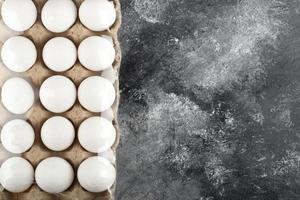 Œufs de poule crus dans une boîte à œufs sur un fond de marbre photo