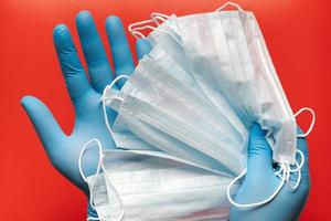 médecin détient respiratoire chirurgical visage masque dans mains bleu médical gants sur rouge Contexte photo
