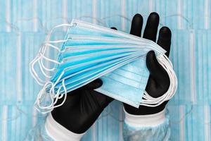 médical homme détient lot bleu chirurgical visage masques dans noir protecteur gant dans mains. concept quarantaine, pandémie épidémie, hygiène photo
