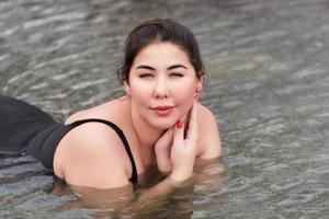 démesuré Jeune brunette adulte modèle dans noir baignade maillot de bain mensonge vers le bas et relaxation dans spa bassin photo