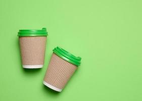 marron jetable café et thé tasses fabriqué de ondulé papier carton avec vert Plastique couvercles sur vert arrière-plan, Haut vue photo