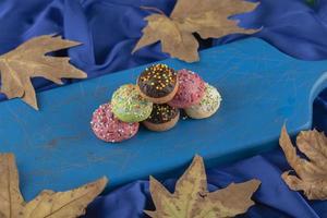 Petits beignets sucrés colorés sur une planche de bois bleue photo