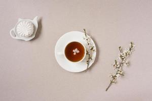 le concept de printemps. une tasse de noir thé avec Pomme fleurs et guimauves sur une théière assiette sur une beige Contexte photo