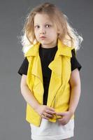 magnifique peu blond fille dans une Jaune veste sur une gris Contexte. cinq année vieux fille. modèle tests pour une enfant. photo