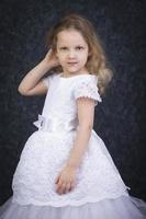 mignonne peu blond fille dans une magnifique blanc robe sur une foncé Contexte. six année vieux magnifique fille photo
