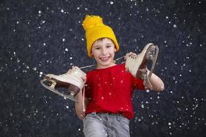 Beau peu garçon dans une tricoté Jaune chapeau avec ancien patins sur une gris Contexte. photo