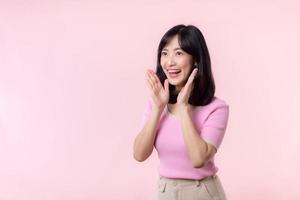 portrait magnifique Jeune asiatique femme expression jaune crier annoncer nouvelles de la communication message ou crier bruyant voix avec main à côté de bouche geste isolé sur rose pastel Contexte. photo